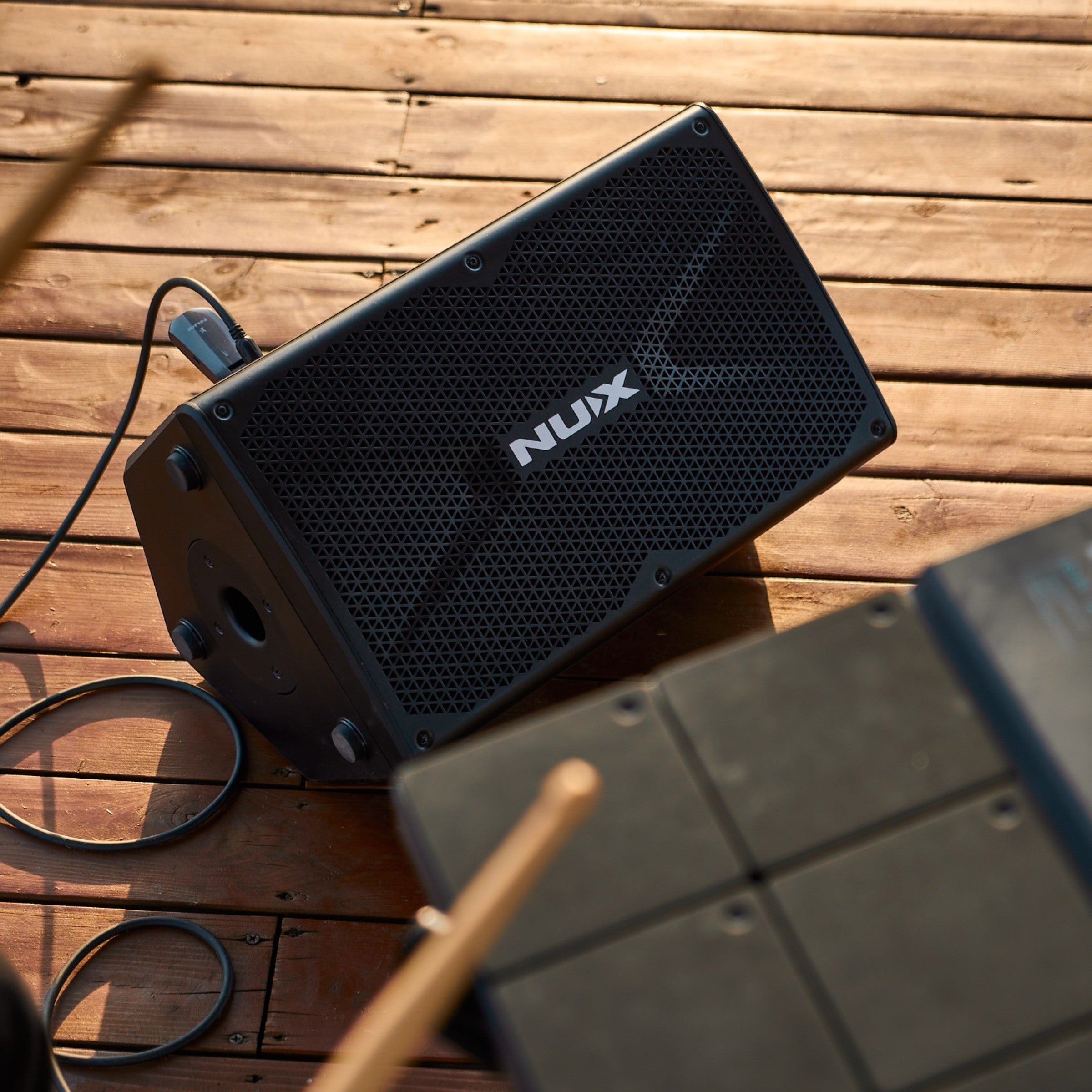Black nux speaker for outdoor use next to a drum pad