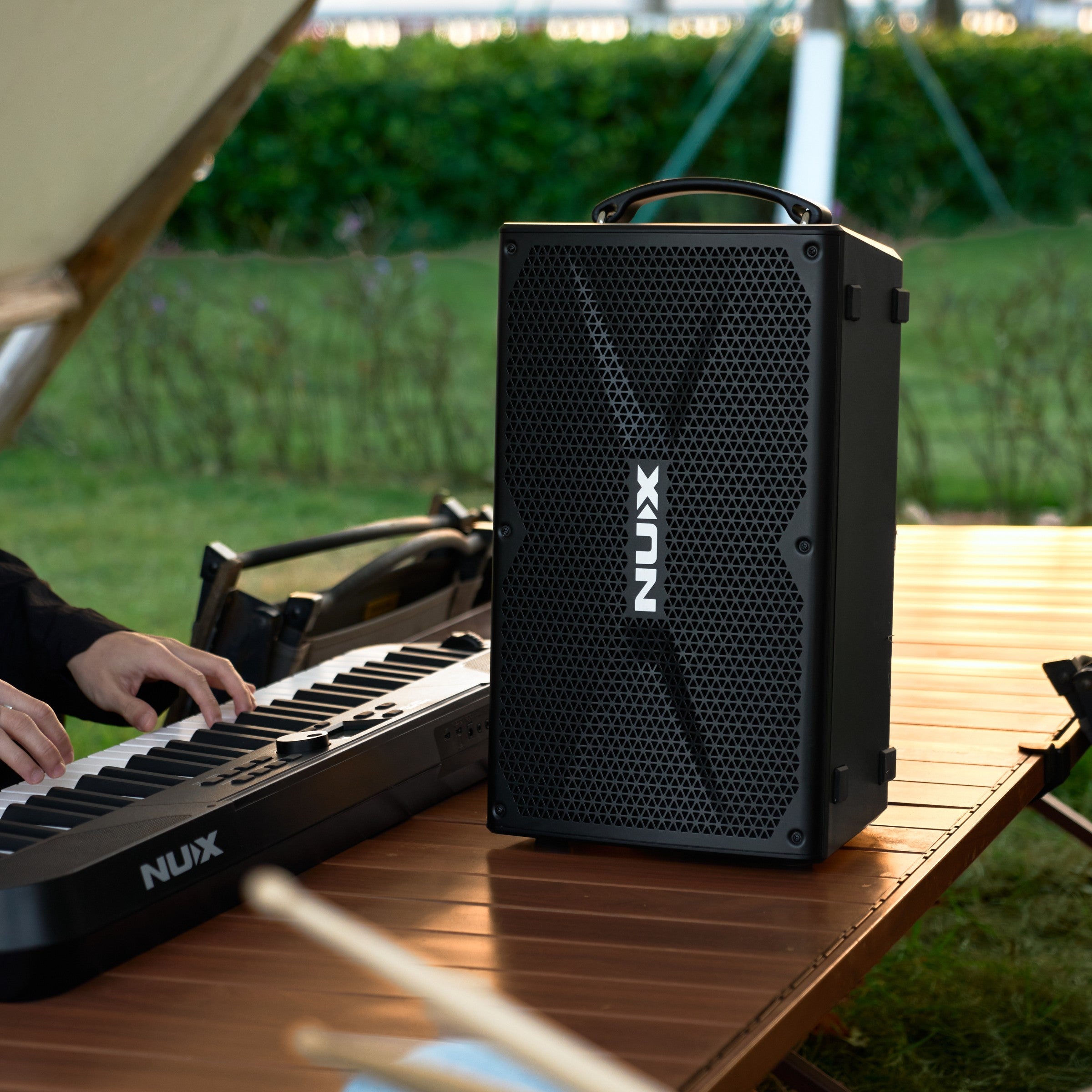 NUX portable speaker on a wooden table with a keyboard, outdoors.