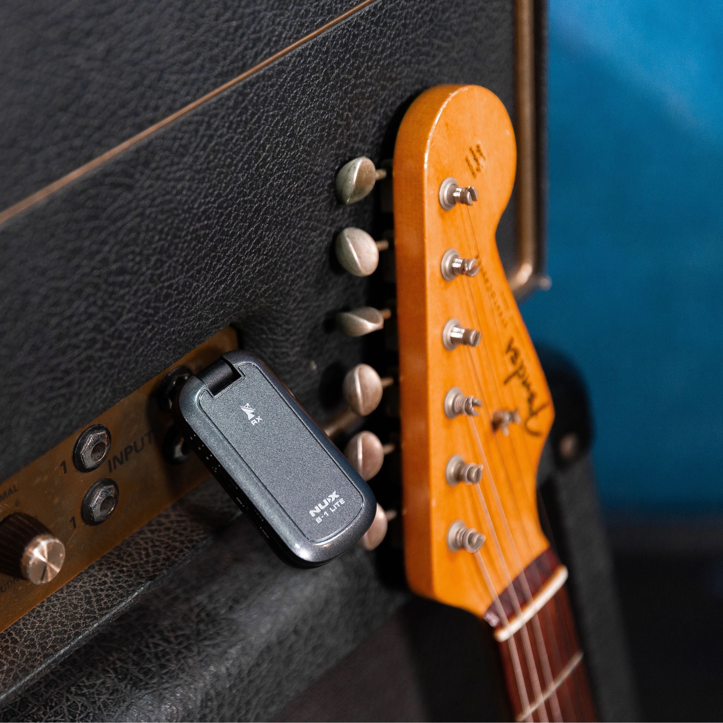 NUX B-1 LITE transmitter plugged in an amp next to a guitar