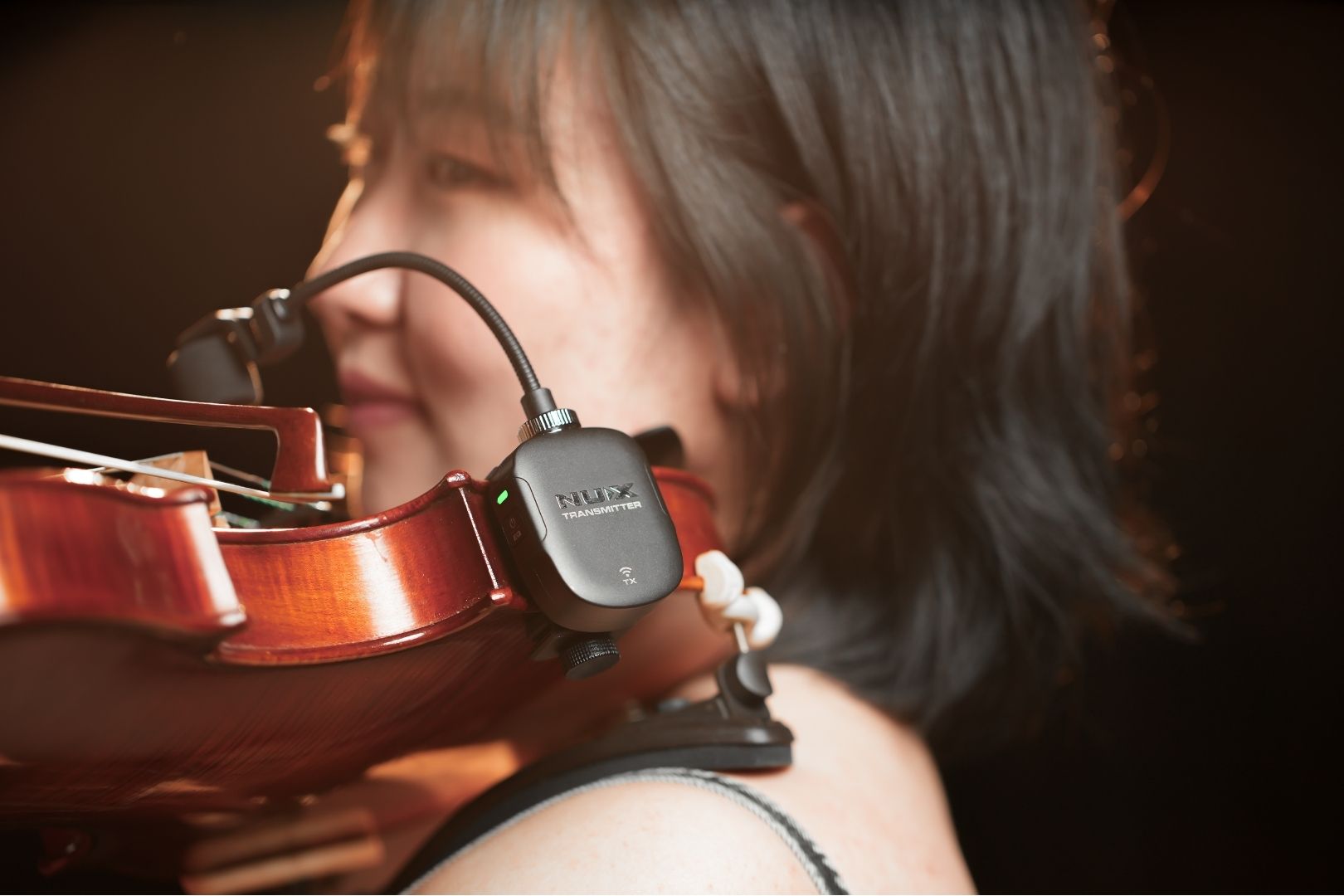 Person holding a violin with a NUX device attached, against a dark background