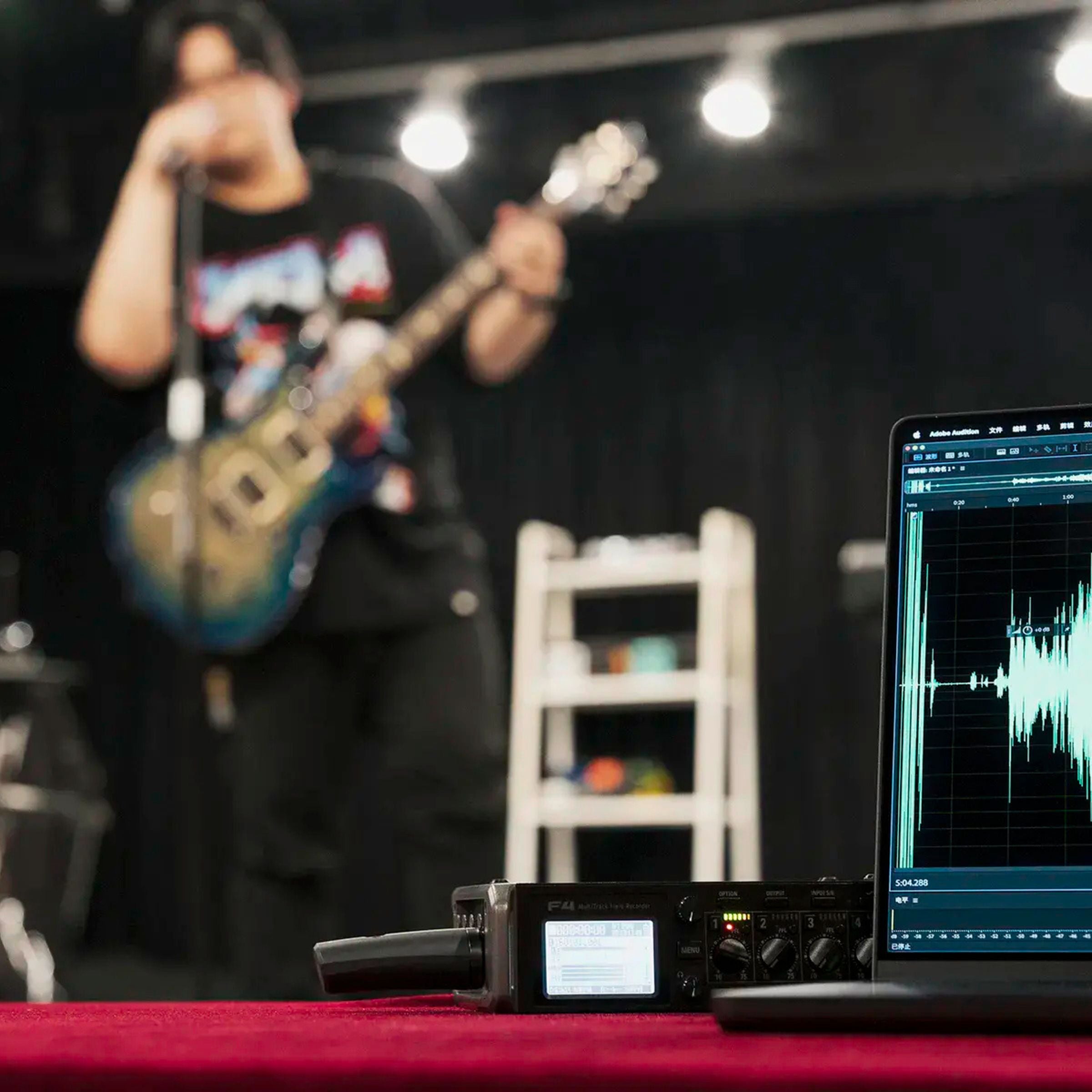Musician singing using NUX B-3RC wireless microphone while playing guitar with recording equipment on a table in the foreground
