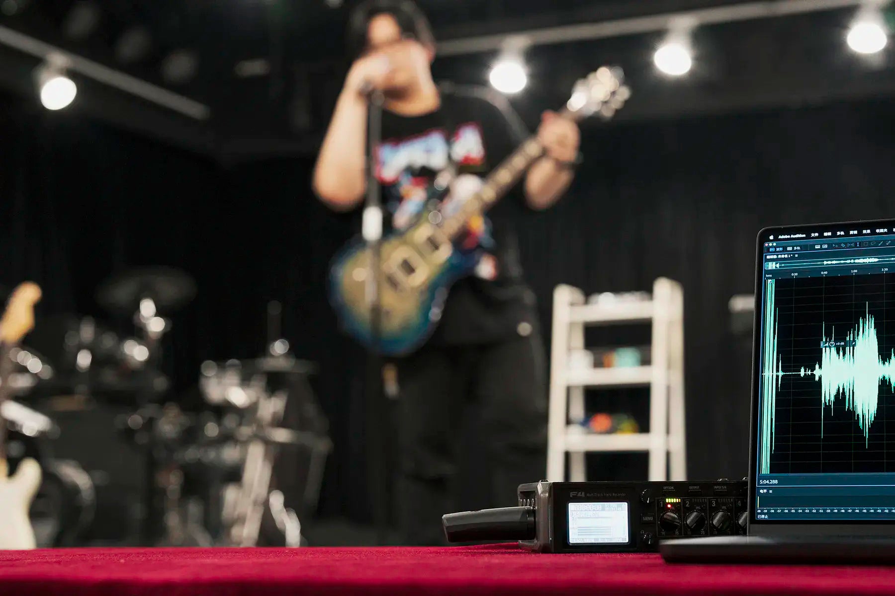 Person playing guitar on stage using NUX B-3RC wireless microphone with audio equipment and laptop displaying waveforms.