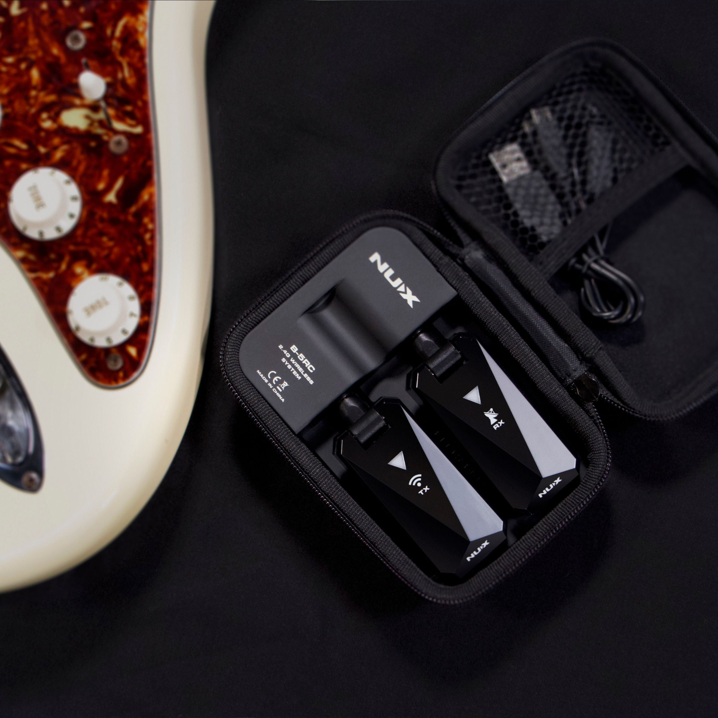 NUX B-5RC wireless guitar system in a portable charging case next to an electric guitar in white background.