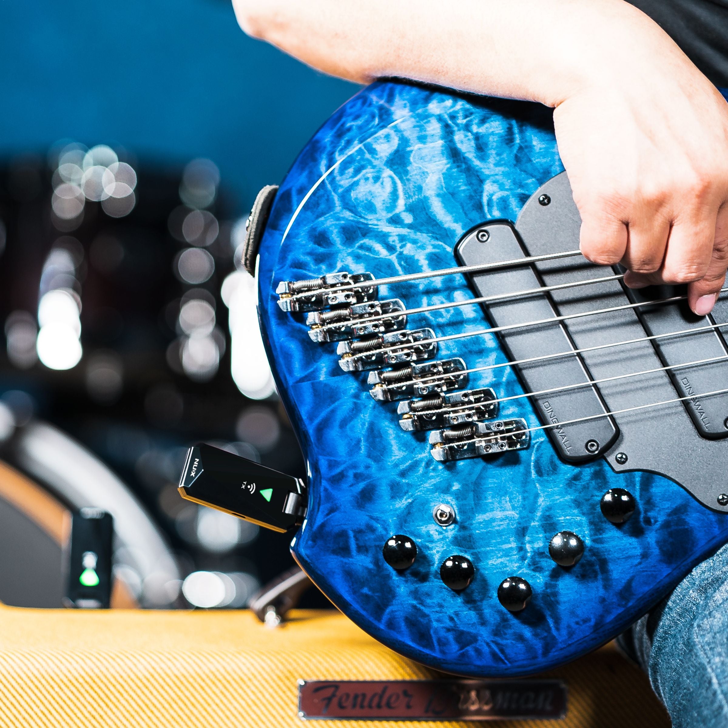 Blue electric bass guitar held by a person with NUX B-5RC transmitter plugged in and the receiver plugged into the amp