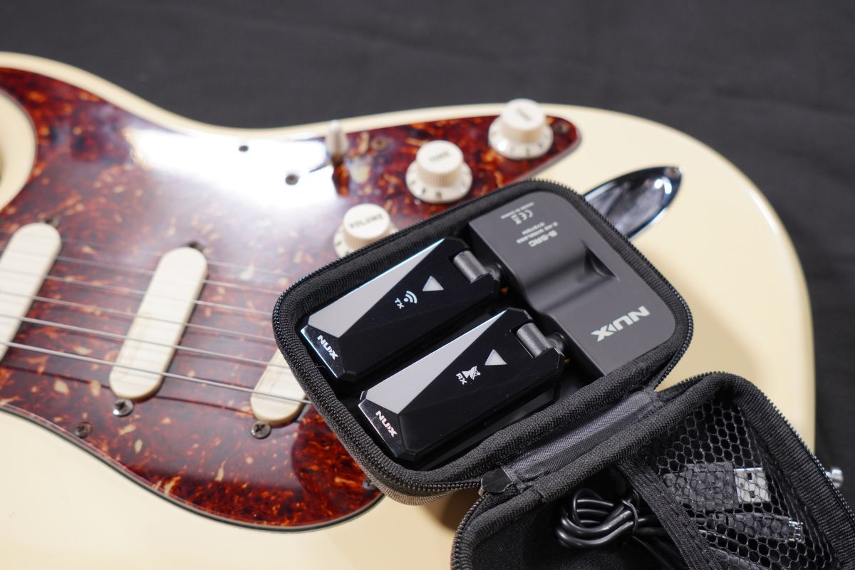 NUX B-5RC charging case with both the transmitter and receiver stored while charging on top of an electric guitar.