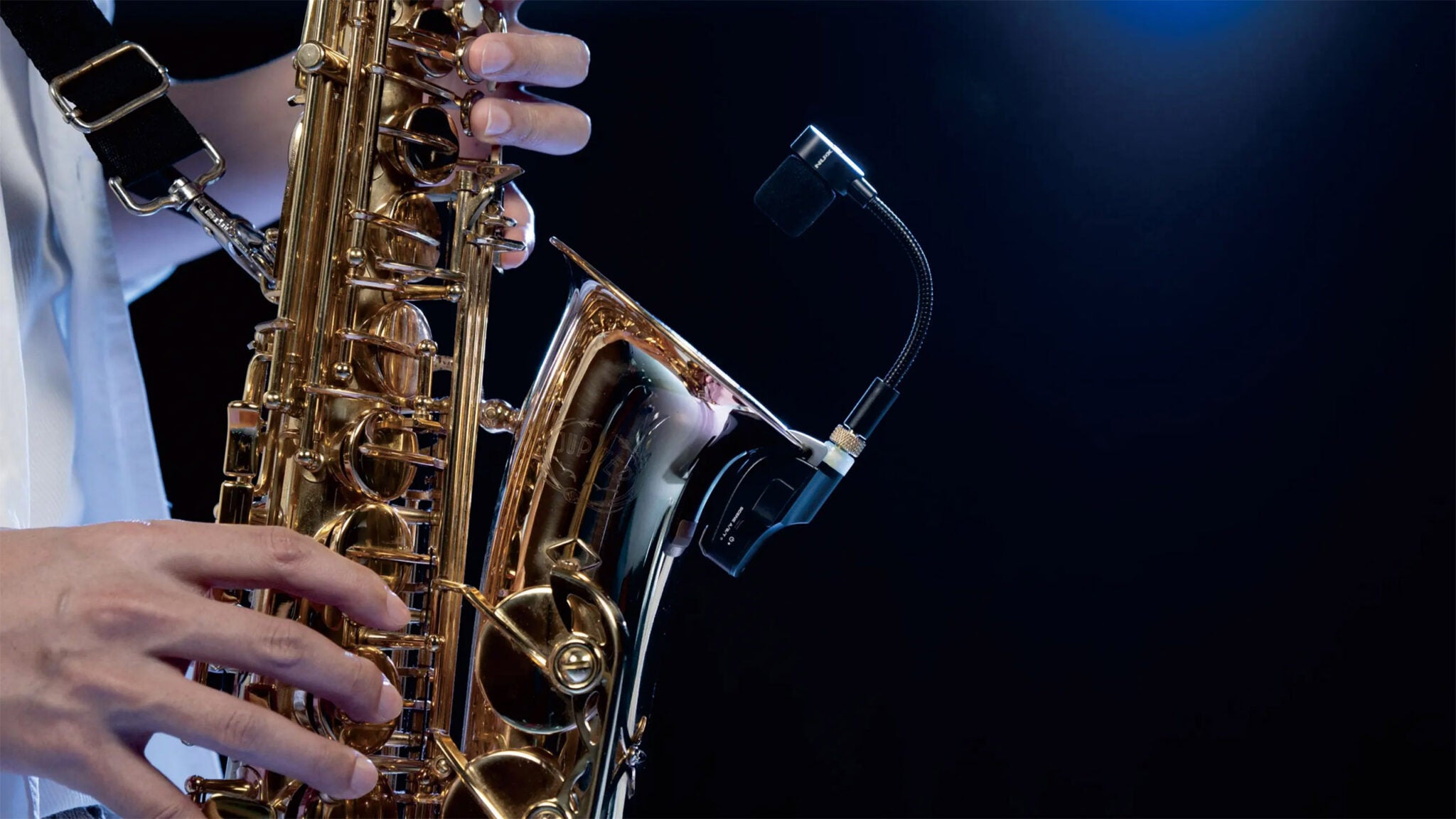 Close-up of a person playing a saxophone against a dark background with NUX B-6 wireless wind instrument microphone attached on the rim.