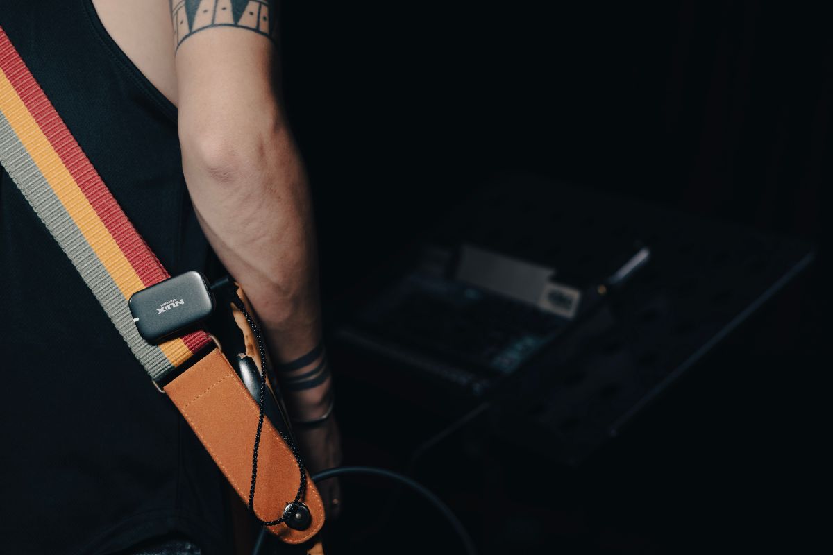 Close up of person wearing a guitar strap with NUX B-7 PSM receiver clipped on.
