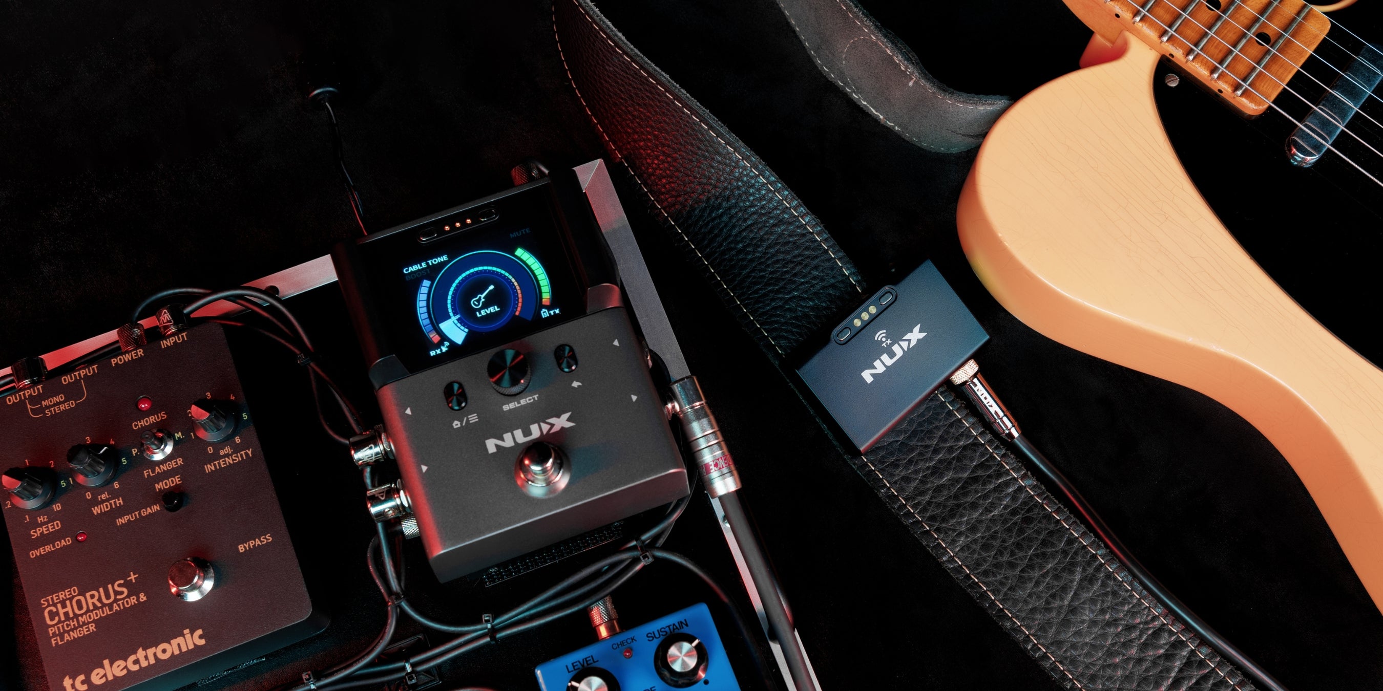 Guitar effects pedals connected to NUX B-8 pedal receiver with the transmitter clipped on to the guitar strap.