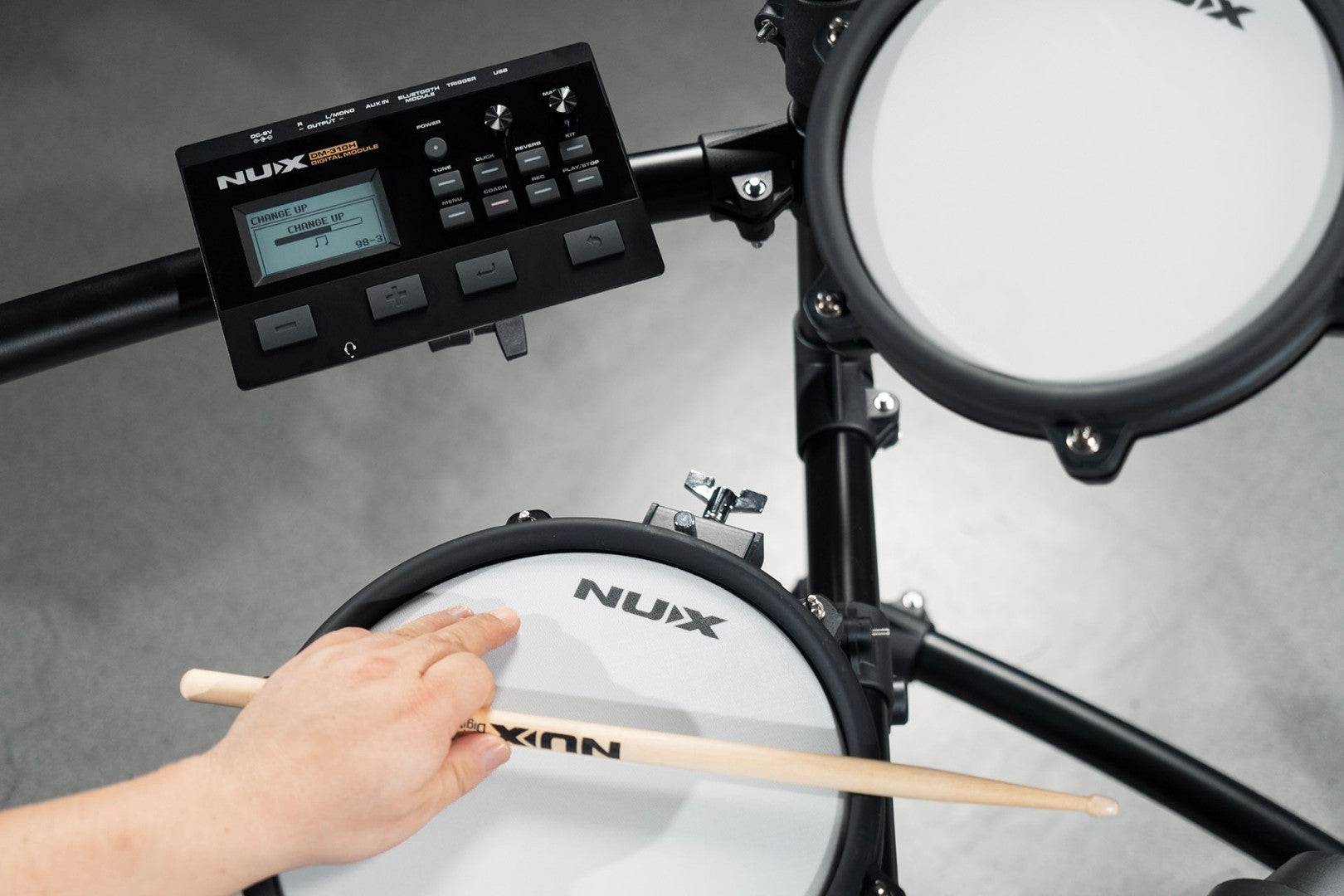 Nux electronic drum set with a hand holding a drumstick on a gray background