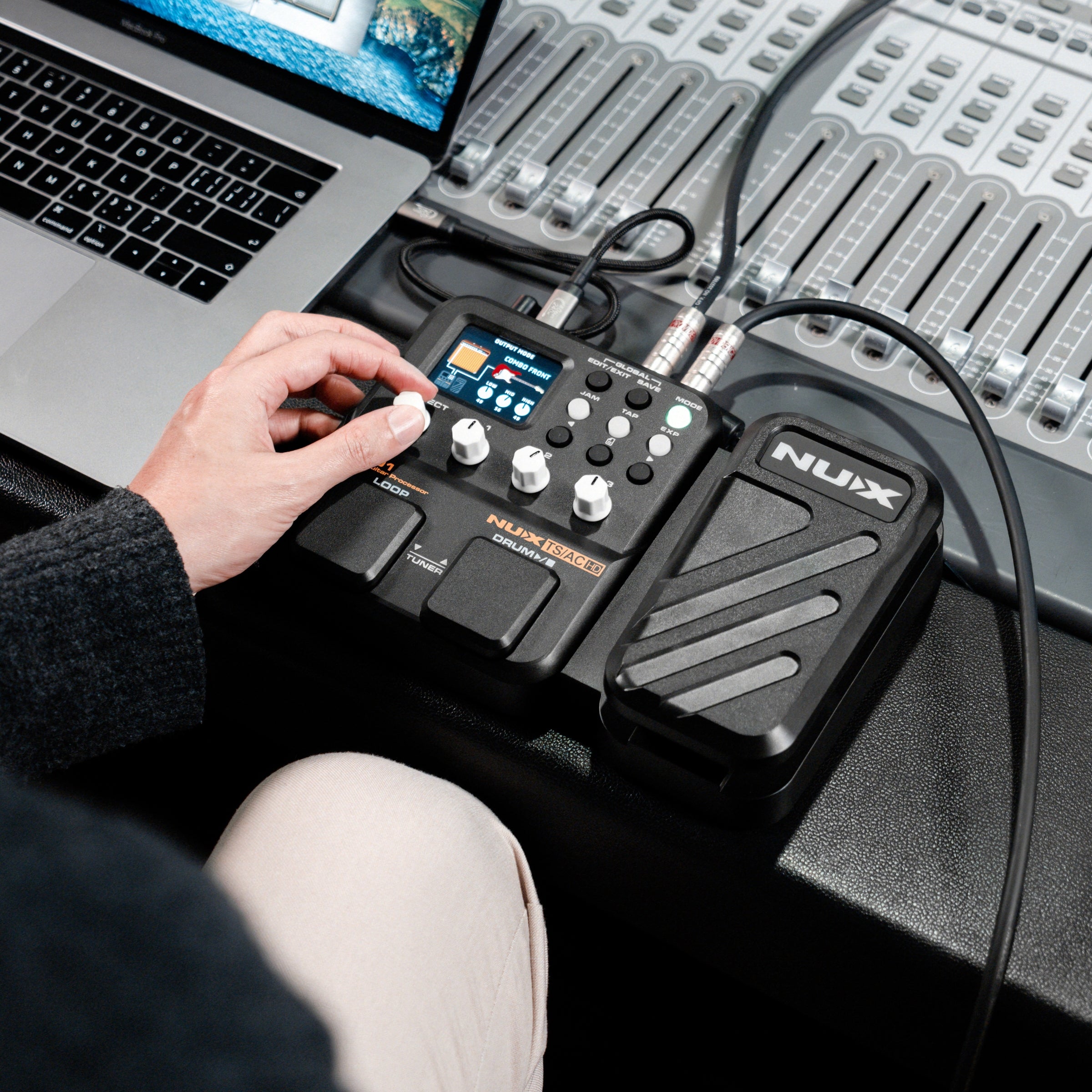 Person using a NUX MG-101 pedal with a laptop and mixing console in the background
