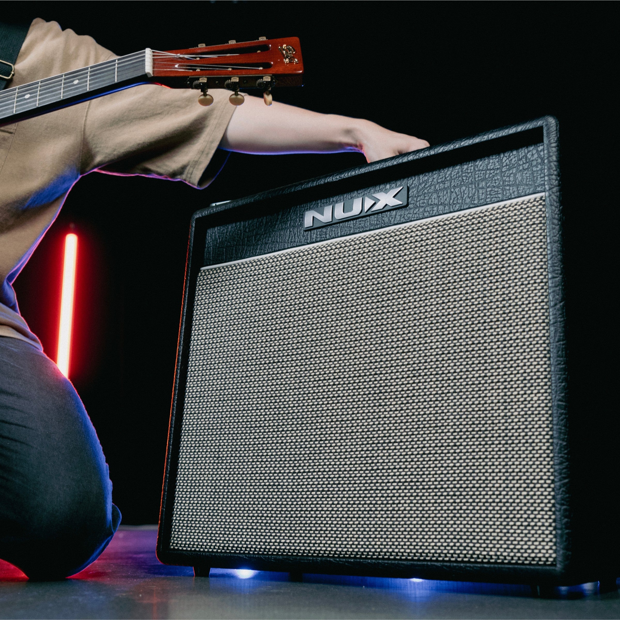 Person holding a guitar above a Nux amplifier on a dark background