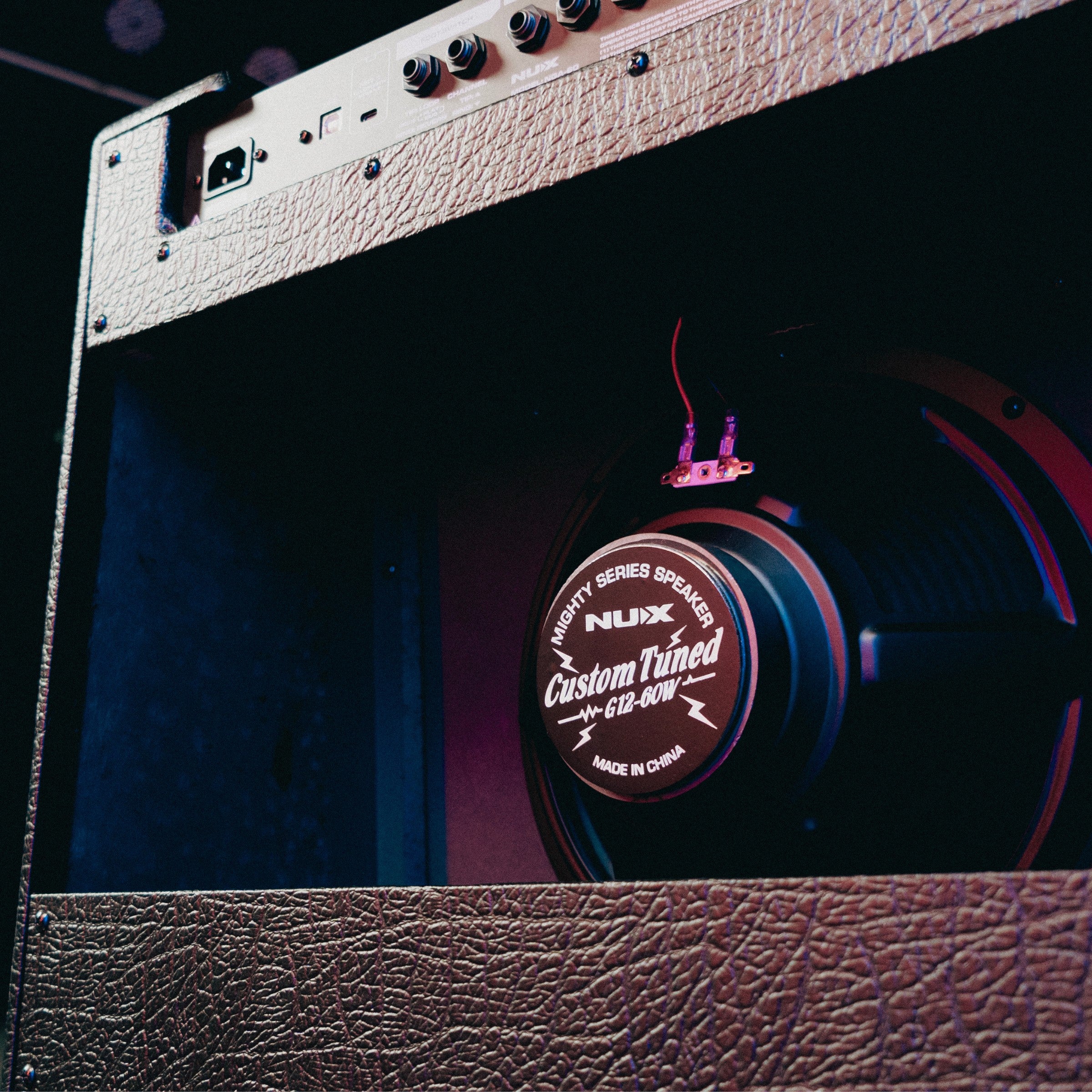 Guitar amplifier with Nux speaker labeled 'Custom Tuned' on a dark background