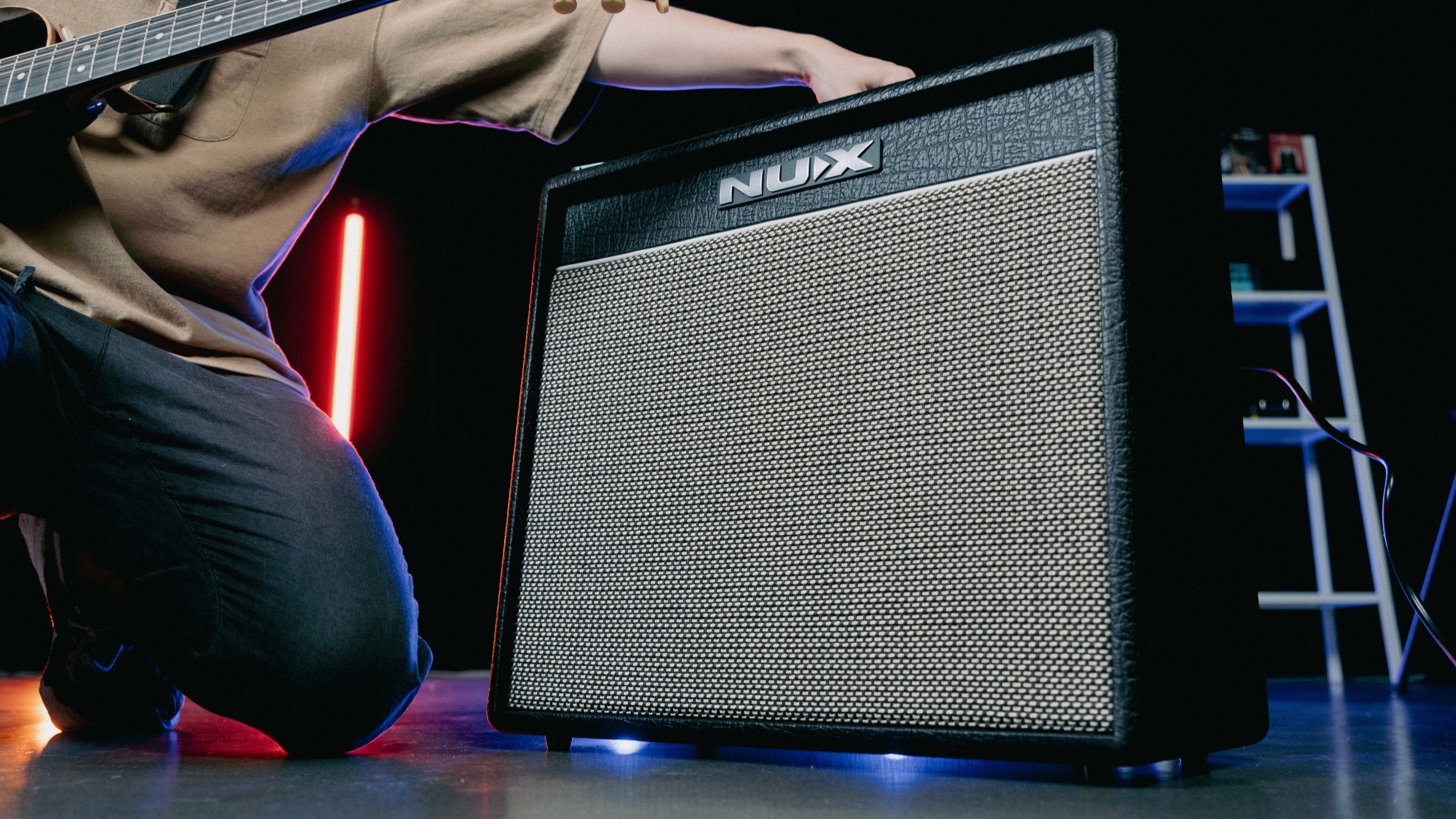 Person playing guitar next to a Nux mighty 40 mk2 amplifier in a dark room