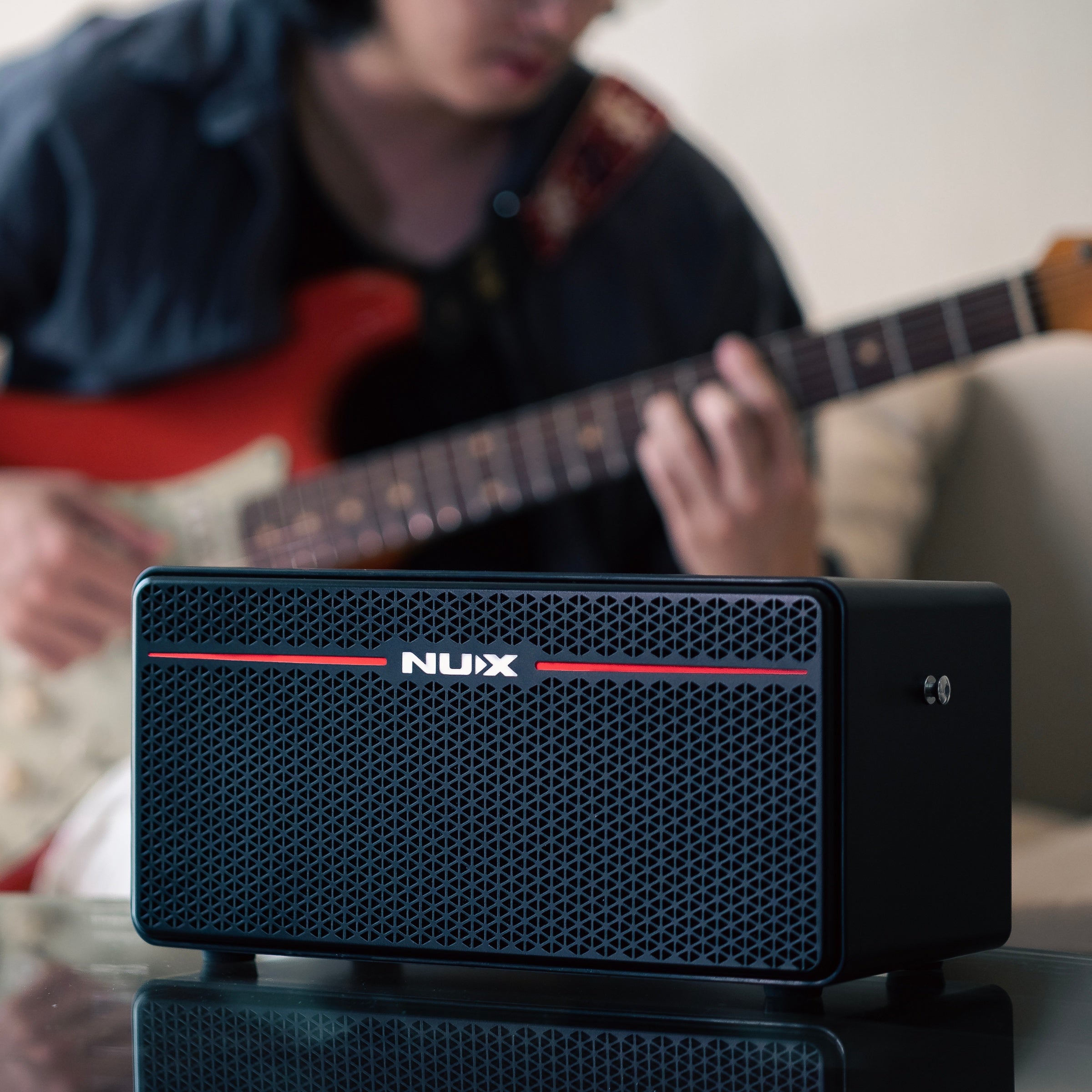Nux mighty space guitar amplifier with a person playing guitar in the background