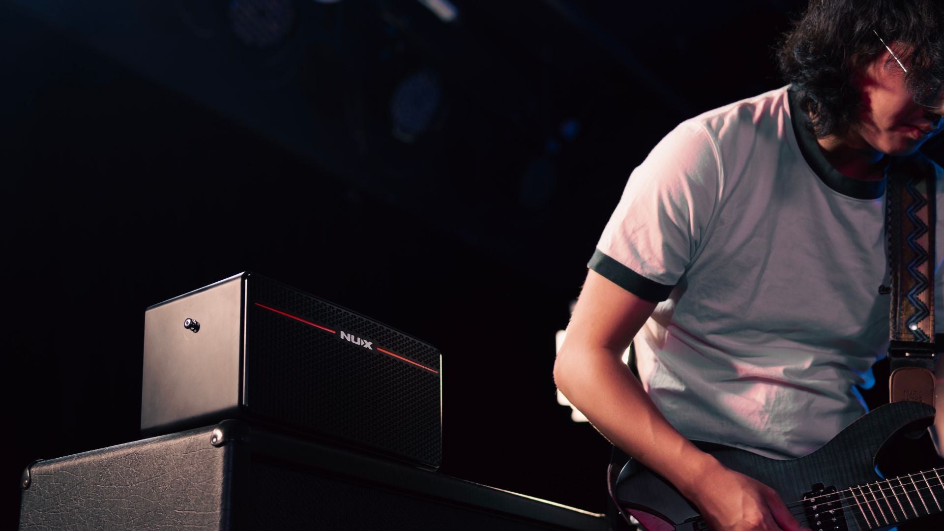 Person playing guitar with a Mighty Space AMP on a stand in a dark setting