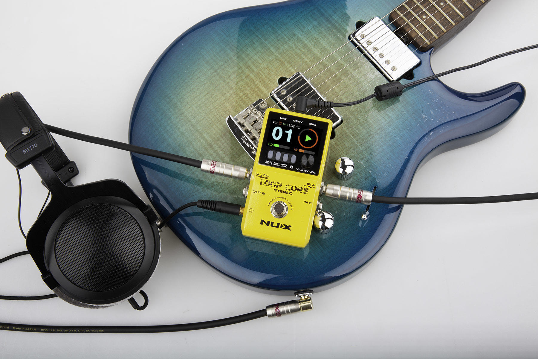 Blue electric guitar with a NUX Loop Core pedal and headphones on a white background