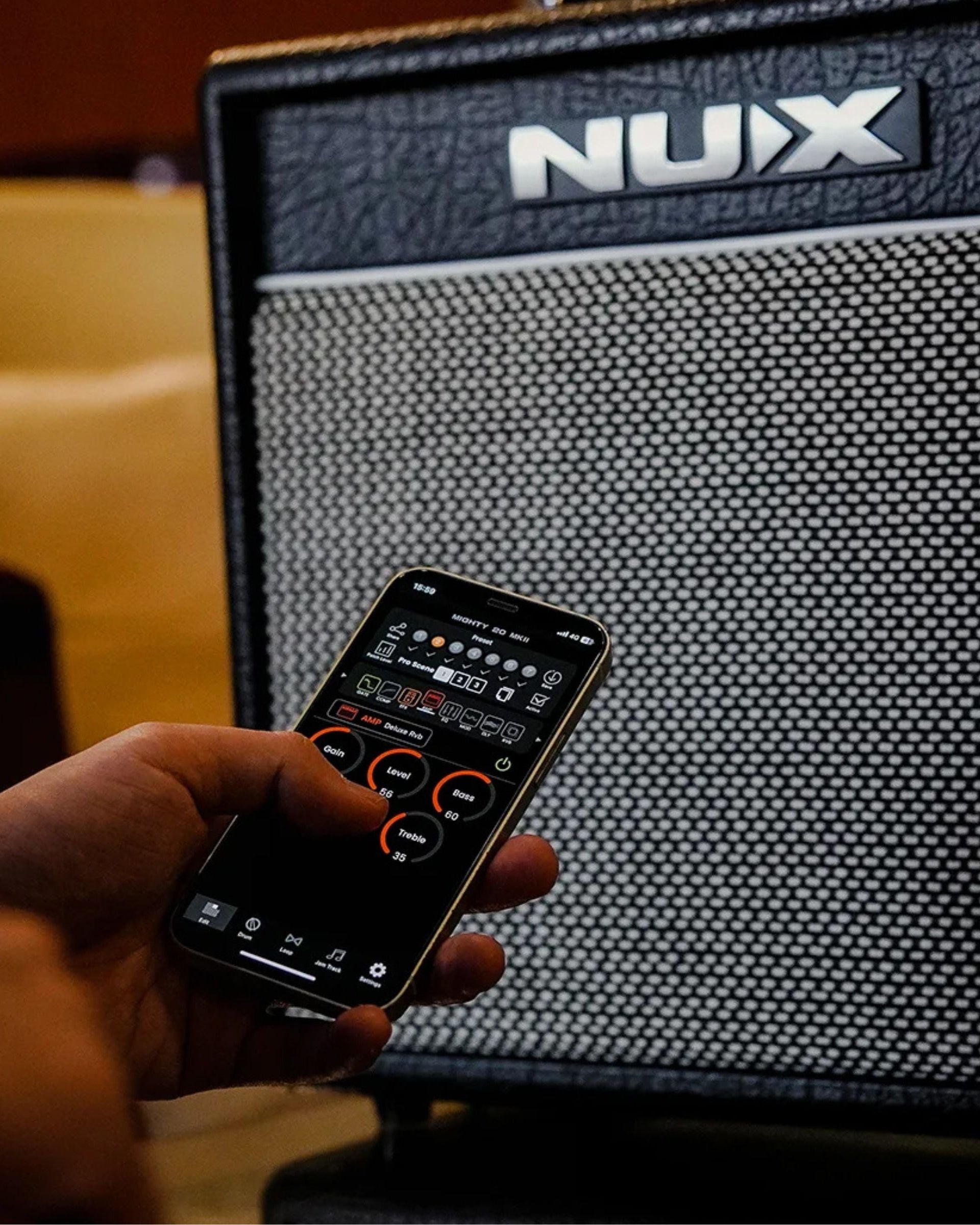 Hand holding phone next to NUX amp showing bluetooth capabilities through nux amp app