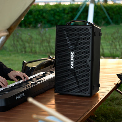 NUX portable speaker on a wooden table with a keyboard, outdoors.