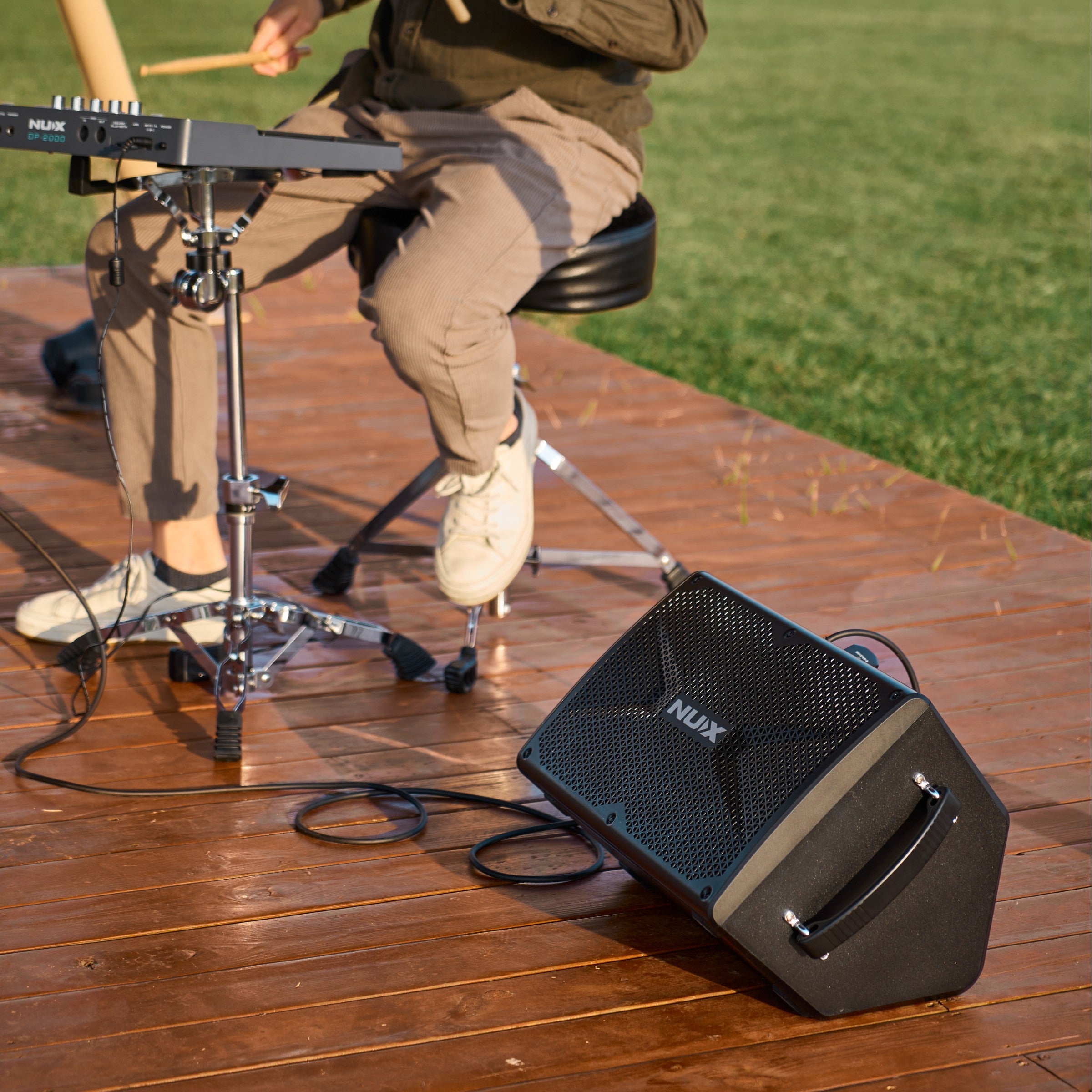 Person playing drumpad with a NUX amplifier on a wooden deck