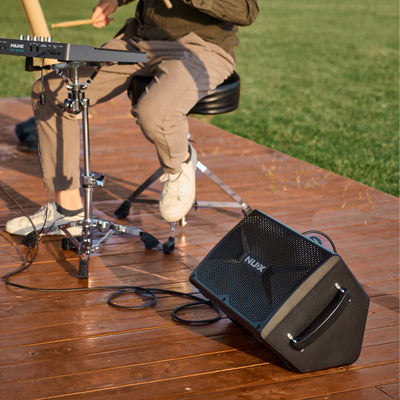 Person playing drumpad with a NUX amplifier on a wooden deck