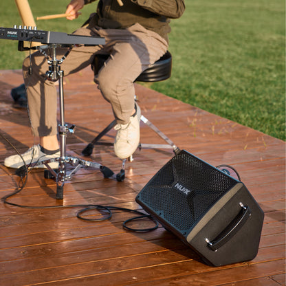 Person playing drumpad with a NUX amplifier on a wooden deck