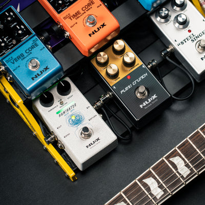 Collection of NUX guitar effect pedals on a dark surface with a guitar neck in the foreground.