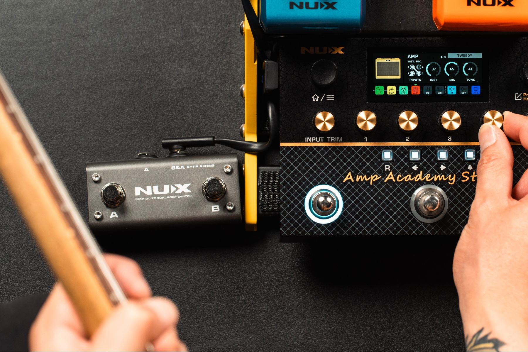 Nux guitar effects pedals on a black surface with a hand holding a guitar.
