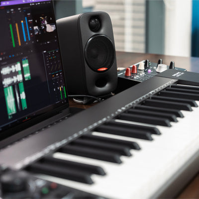 Music production setup with keyboard, laptop, and a NUX Studio Monitor speaker on a desk.