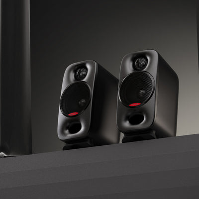 Pair of black nux studio speakers on a dark surface with a dark background
