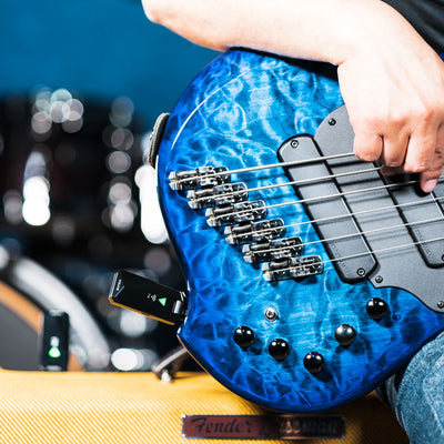 Blue electric bass guitar held by a person with NUX B-5RC transmitter plugged in and the receiver plugged into the amp