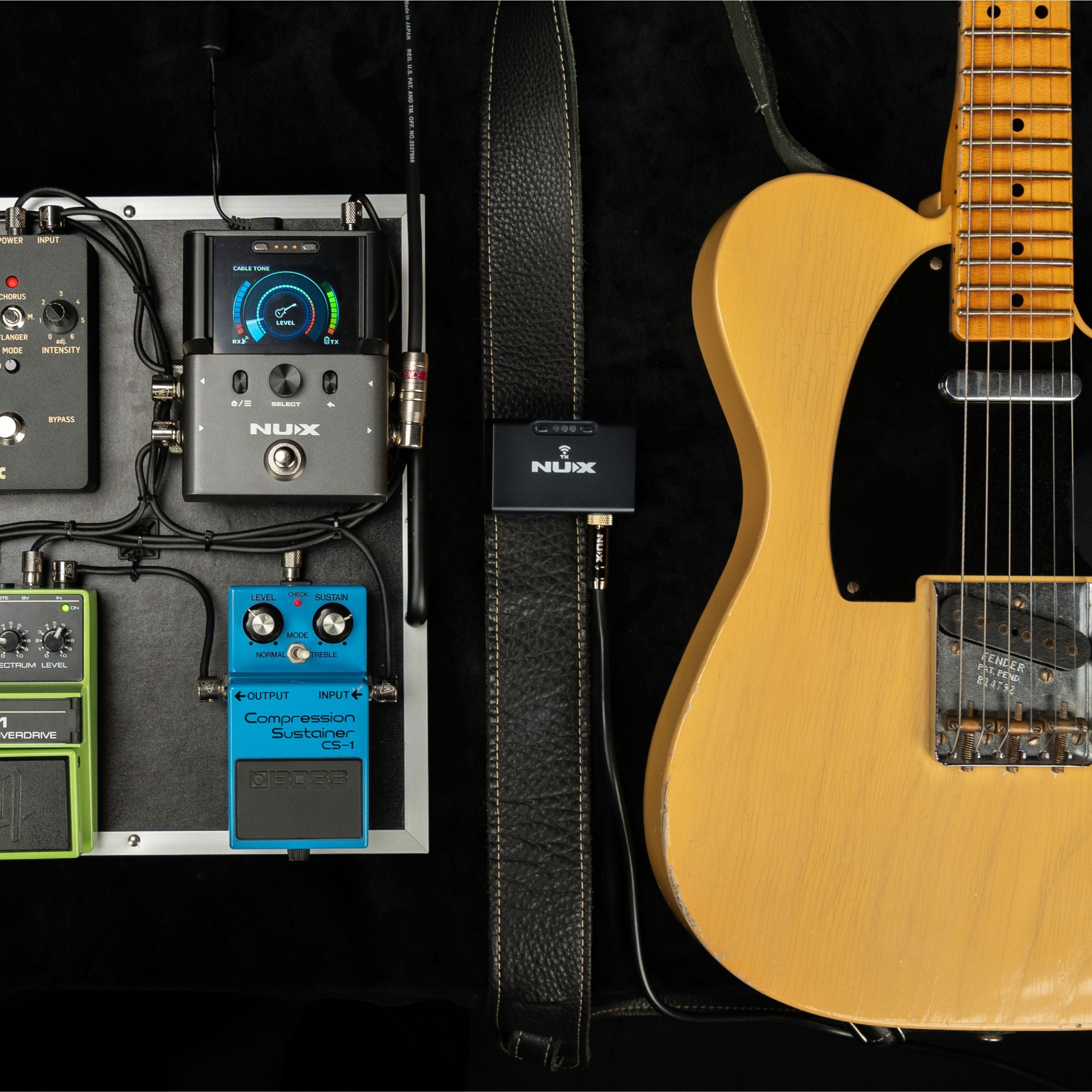 Guitar with effects pedals connected to NUX B-8 receiver and the transmitter clipped on the guitar strap on a dark background