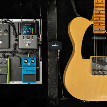 Guitar with effects pedals connected to NUX B-8 receiver and the transmitter clipped on the guitar strap on a dark background