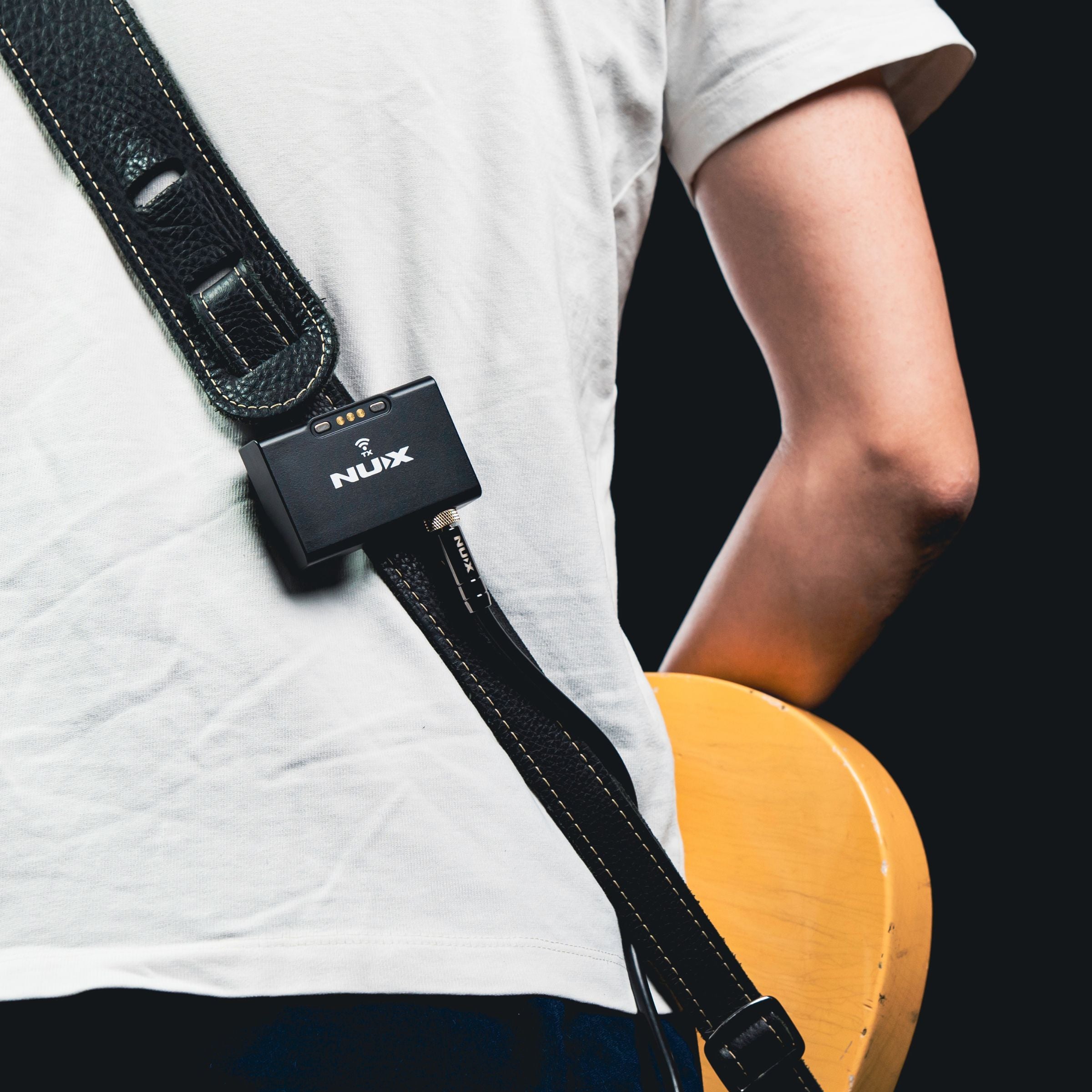 Person holding a guitar with a NUX B-8 transmitter device attached to the strap on a black background