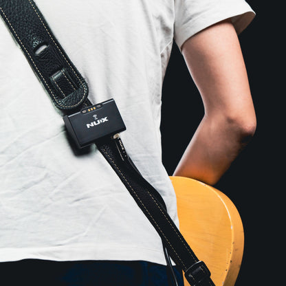 Person holding a guitar with a NUX B-8 transmitter device attached to the strap on a black background