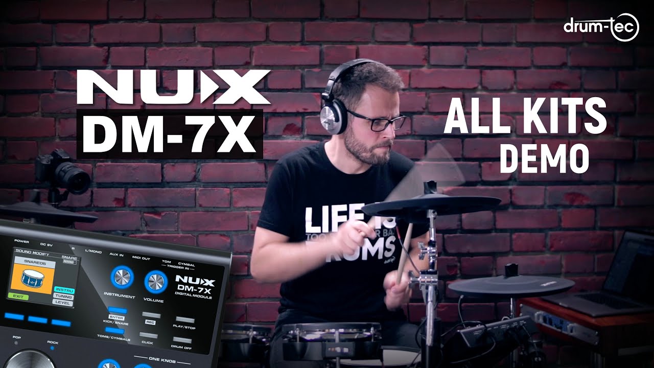 Man playing a drum set with NUX DM-7X equipment in front of a brick wall.