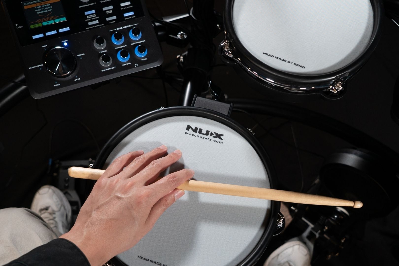 Person playing a NUX electronic drum set with a close-up of the drums and control panel.