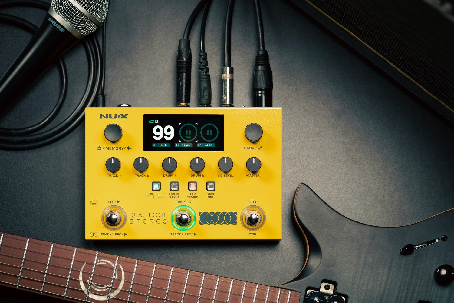 Yellow NUX dual loop stereo pedal stompbox on a dark surface next to a mic and an electric guitar