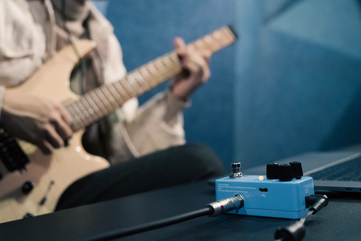 Person playing guitar with a NUX DRUM & LOOP HOOK effects pedal on a table