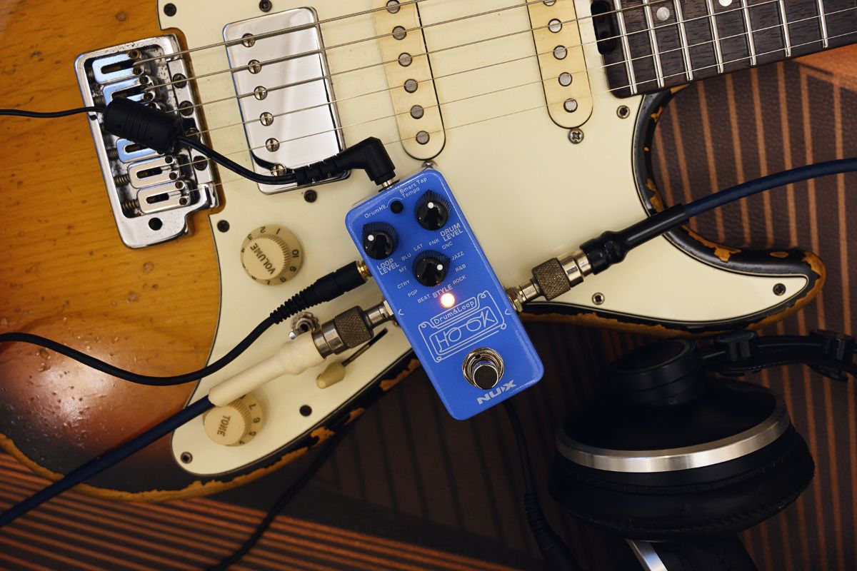 Guitar with a NUX HOOK DRUM & LOOP blue effects pedal and headphones on a wooden surface