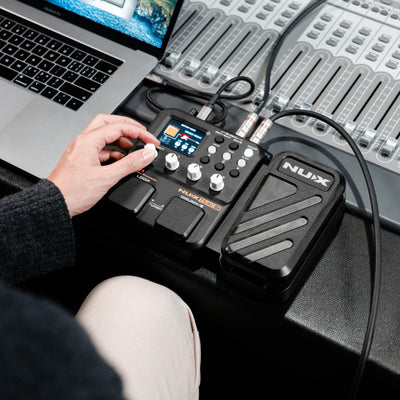 Person using a NUX MG-101 pedal with a laptop and mixing console in the background