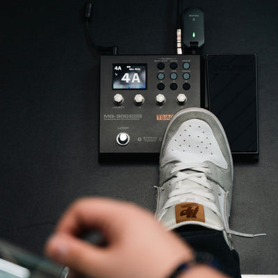Person using a NUX MG-300 MKII guitar effects pedal with a digital display on a dark surface
