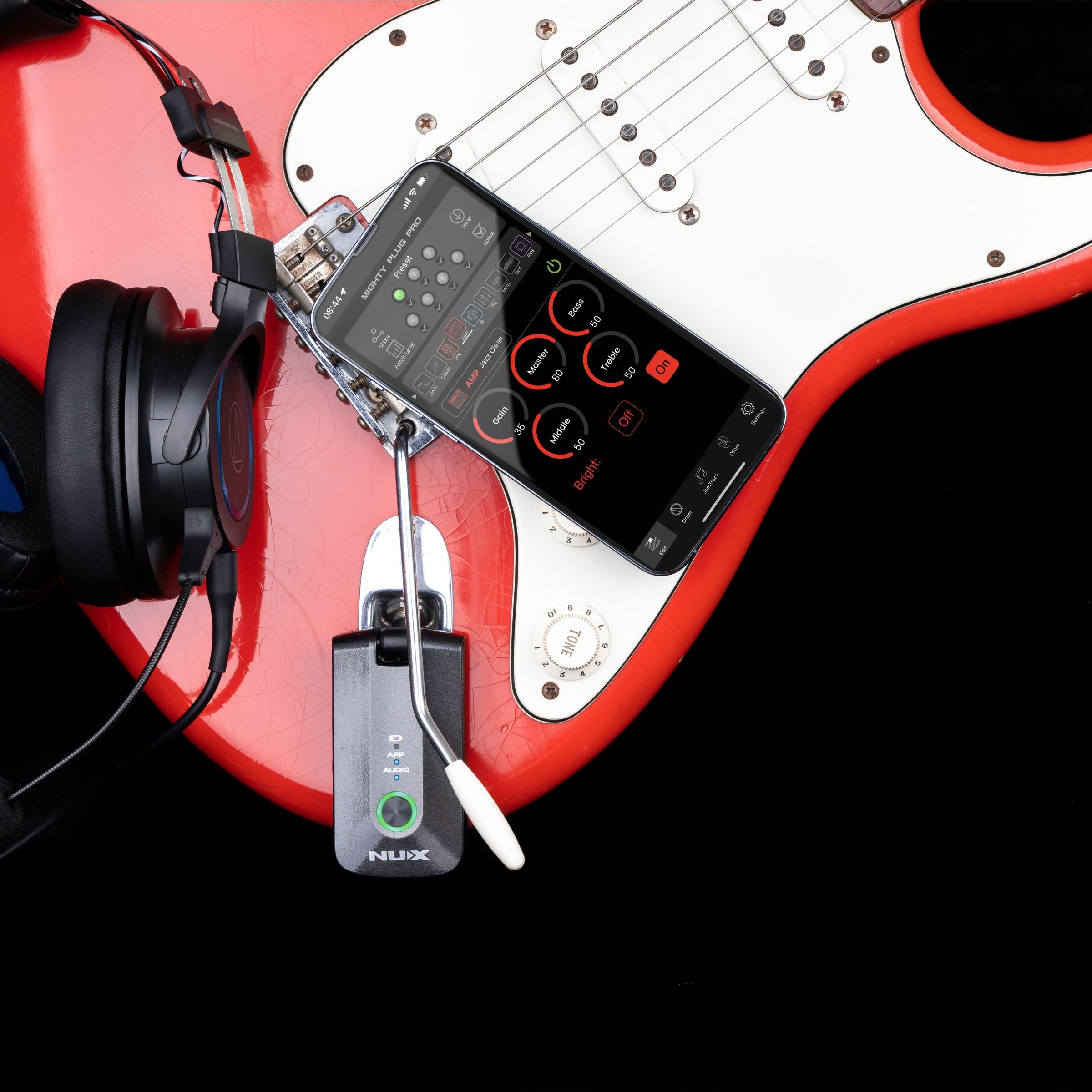 Red electric guitar with a smartphone, NUX Mighty Plug Pro plugged, and headphones on a black background