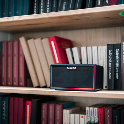 NUX Bluetooth speaker on a bookshelf with books around