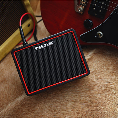 Nux small portable guitar amplifier on a wooden surface with a guitar in the background