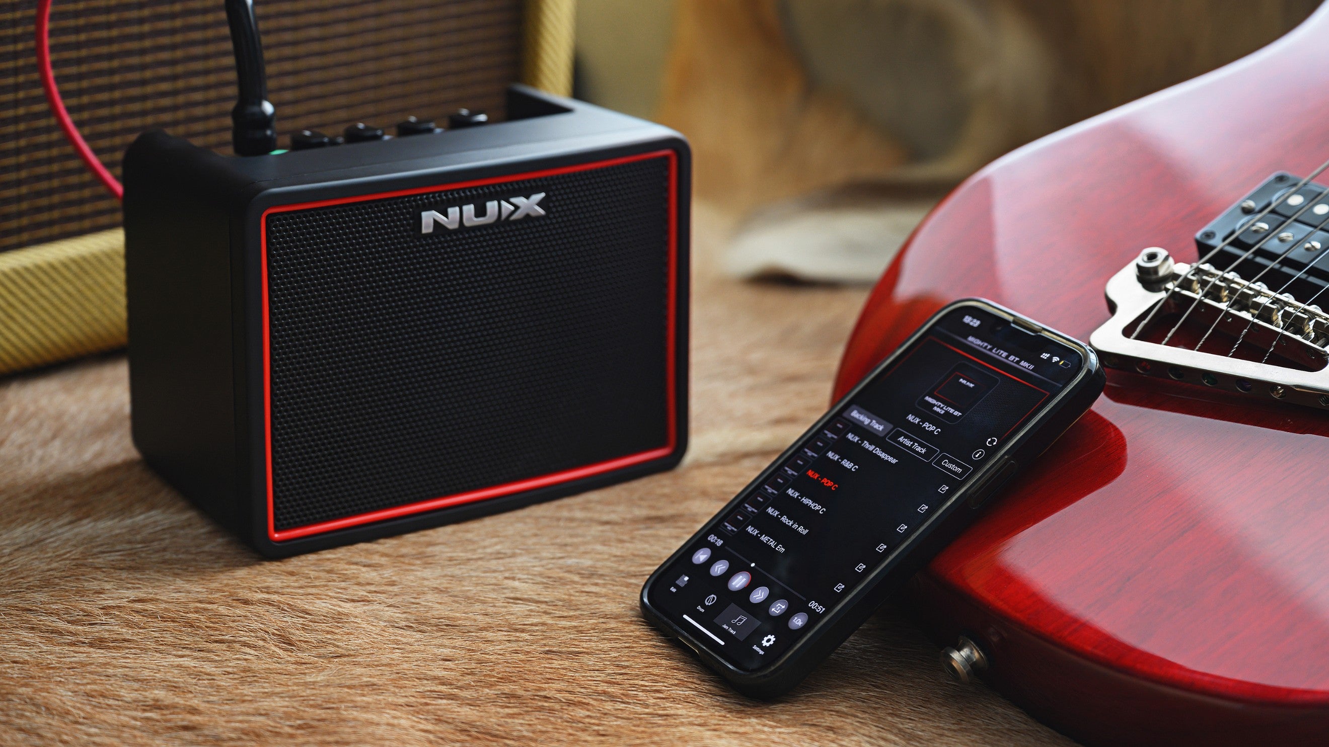 Nux portable guitar amplifier with a smartphone and red electric guitar on a wooden surface