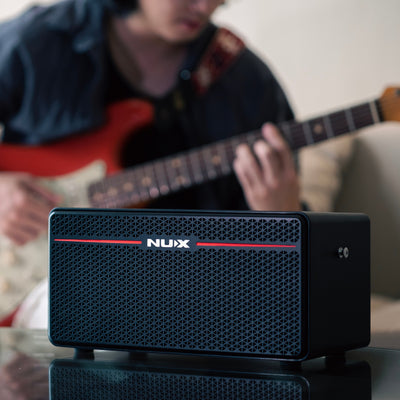 Nux mighty space guitar amplifier with a person playing guitar in the background