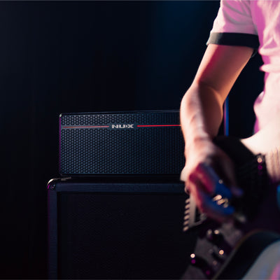 person playing guitar on foreground with nux mighty space guitar amp