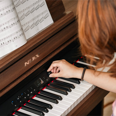 Person playing a NUX digital piano with sheet music in the background