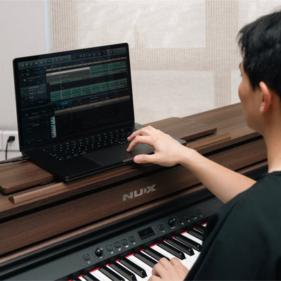 Person using a laptop on a NUX music stand with a piano in the foreground