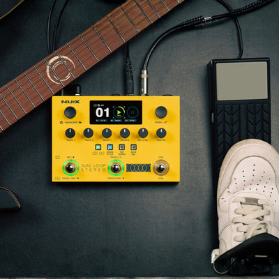 yellow nux dual loop stereo with separate pedal attached next to a guitar